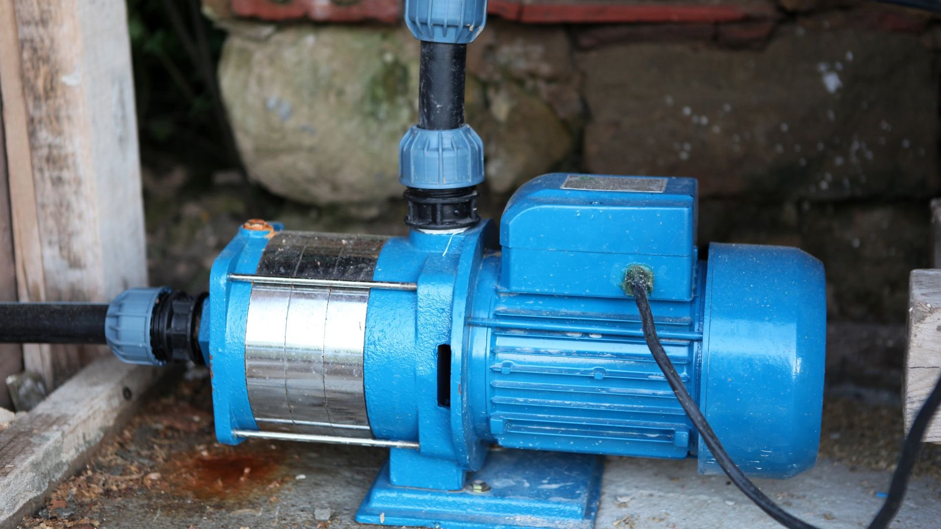 Blue water pump with pipes and electrical cord on concrete surface